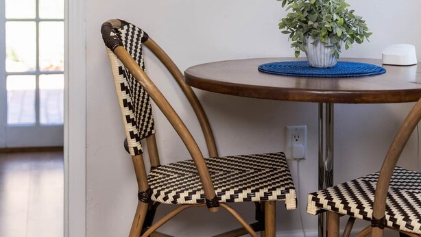 A room with a round table, two wicker chairs, a potted plant, and a framed botanical illustration on the wall. - Chestnut Cottage- Cozy Cottage for Two! (Paso Robles)