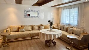 Una sala de estar con un sofá color beige, una mesa redonda y un espejo decorativo en la pared.