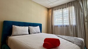 Una habitación de hotel con cama, ventana con cortinas e iluminación empotrada en el techo.