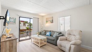 A living room with a sofa, armchair, and a table with a lamp. - Coastal St. Augustine Beach Condo | Partial Ocean View | Resort Amenities | Steps to the Beach | Sleeps 6 (St. Augustine)
