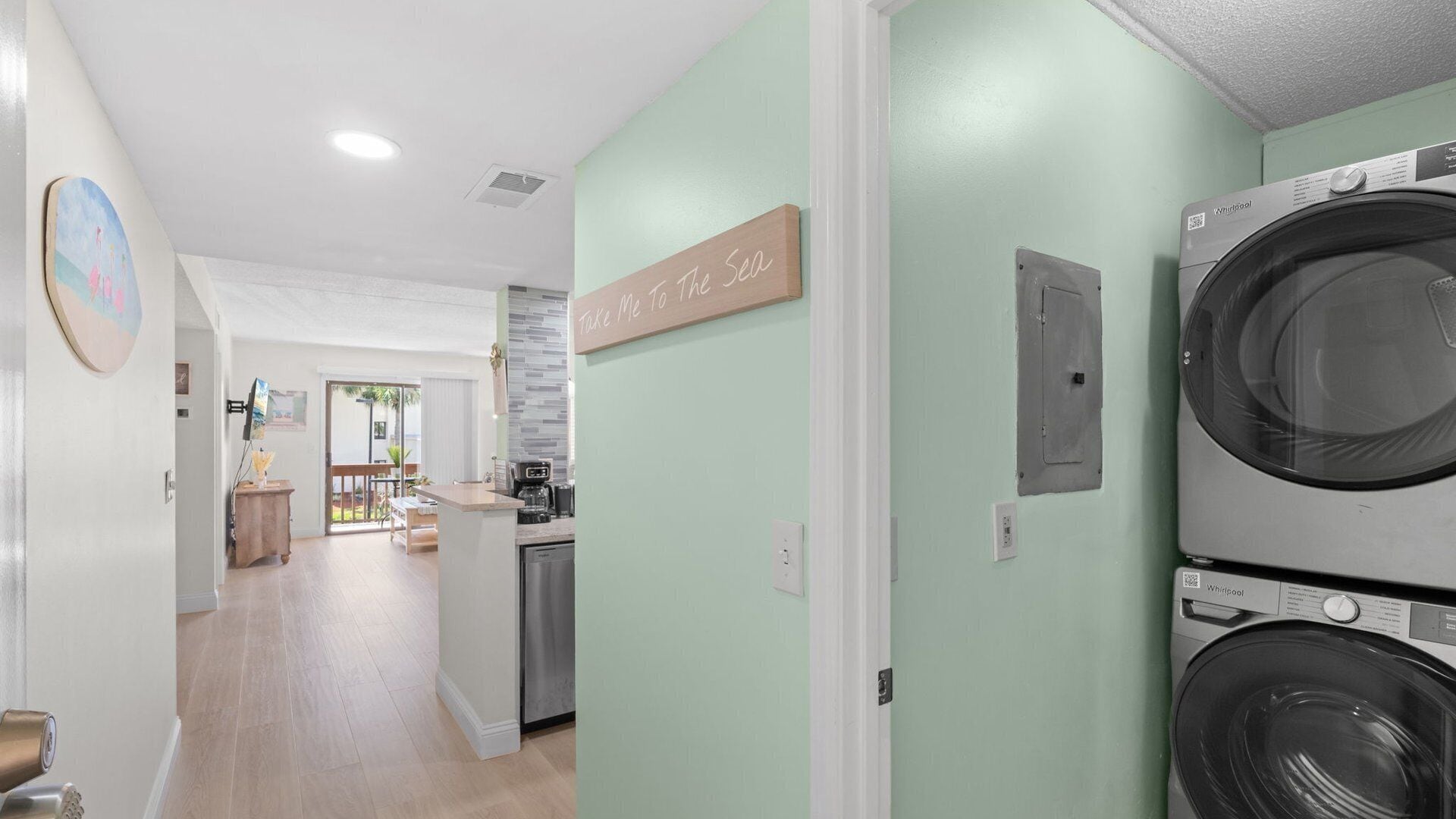 A laundry area with a sign that reads 'Take Me To The Sea' and a Whirlpool washer.