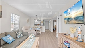 A modern living room with a sofa, a dining area, and a kitchen in the background. - Coastal St. Augustine Beach Condo | Partial Ocean View | Resort Amenities | Steps to the Beach | Sleeps 6 (St. Augustine)