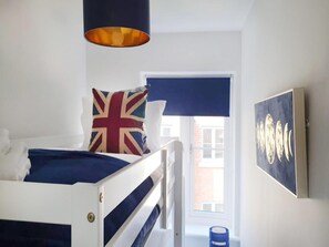 Ein Schlafzimmer mit Etagenbett, Kissen mit Wimpelaufdruck, einem Gemälde und einem Fenster mit Aussicht.