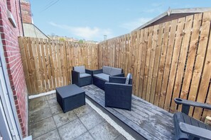 Eine Terrassenfläche mit Gartenmöbeln, darunter eine Couch und Stühle, sowie ein Holzboden.