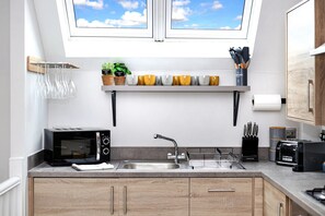 Eine kleine Küche mit integriertem Mikrowellenherd, Spüle und Toaster. Über der Spüle befindet sich ein Fenster und ein Regal mit Blumentöpfen und Küchenutensilien.