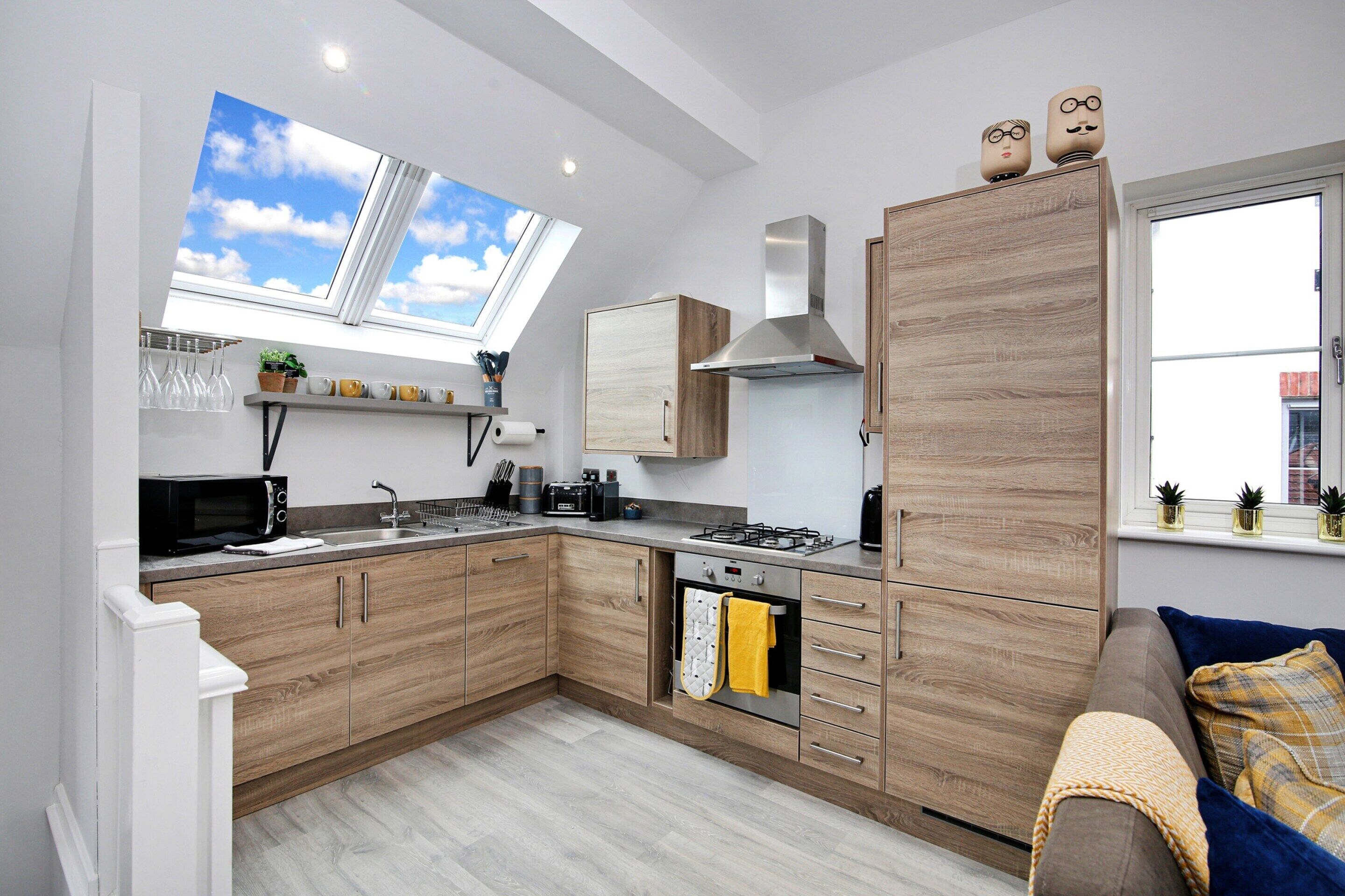 A modern kitchen with wooden cabinets, a built-in oven, and a skylight.