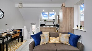 A modern living room with a sofa, a dining area with a table set for four, and a kitchen with a window view. - Holiday Home Near Centre of Whitby (Whitby)