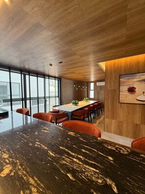 A modern dining area with a large marble table, orange chairs, and a wooden ceiling. - HIT Cabo Branco (João Pessoa)