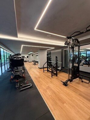 A modern gym with various exercise equipment, large windows, and a wooden floor. - HIT Cabo Branco (João Pessoa)
