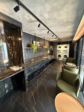 A modern bathroom with a black marble countertop, a sink, and a mirror. There are two green chairs and a wooden table. - HIT Cabo Branco (João Pessoa)