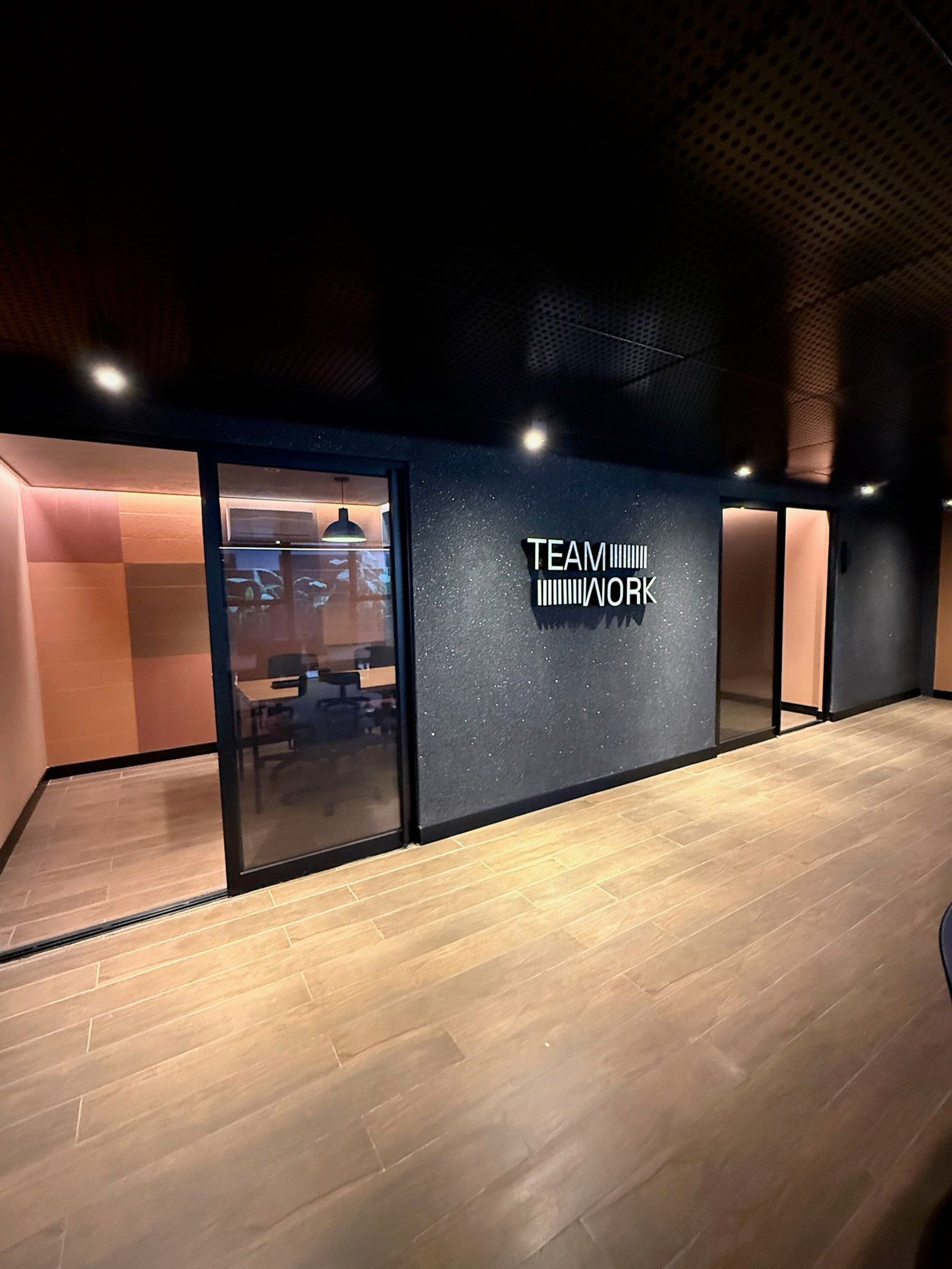 An interior space with a glass partition, a sign reading 'TEAM WORK', and a wooden floor.