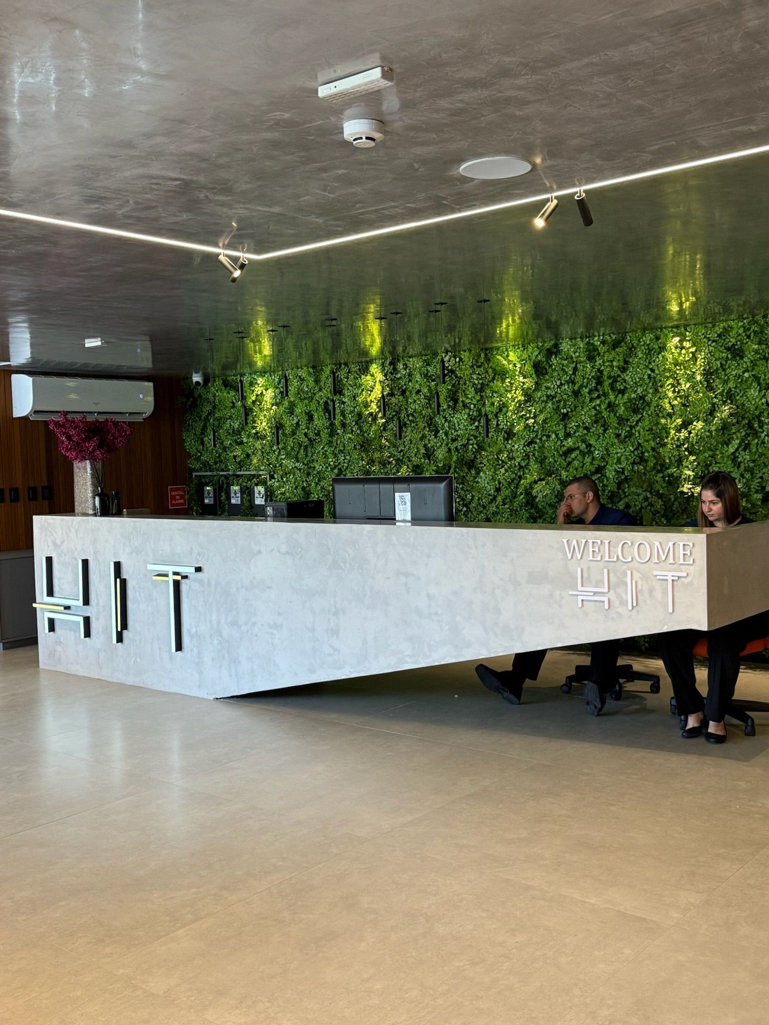 Un comptoir d’accueil avec une pancarte indiquant « BIENVENUE », un mur végétal et un plafond doté d’un éclairage encastré.