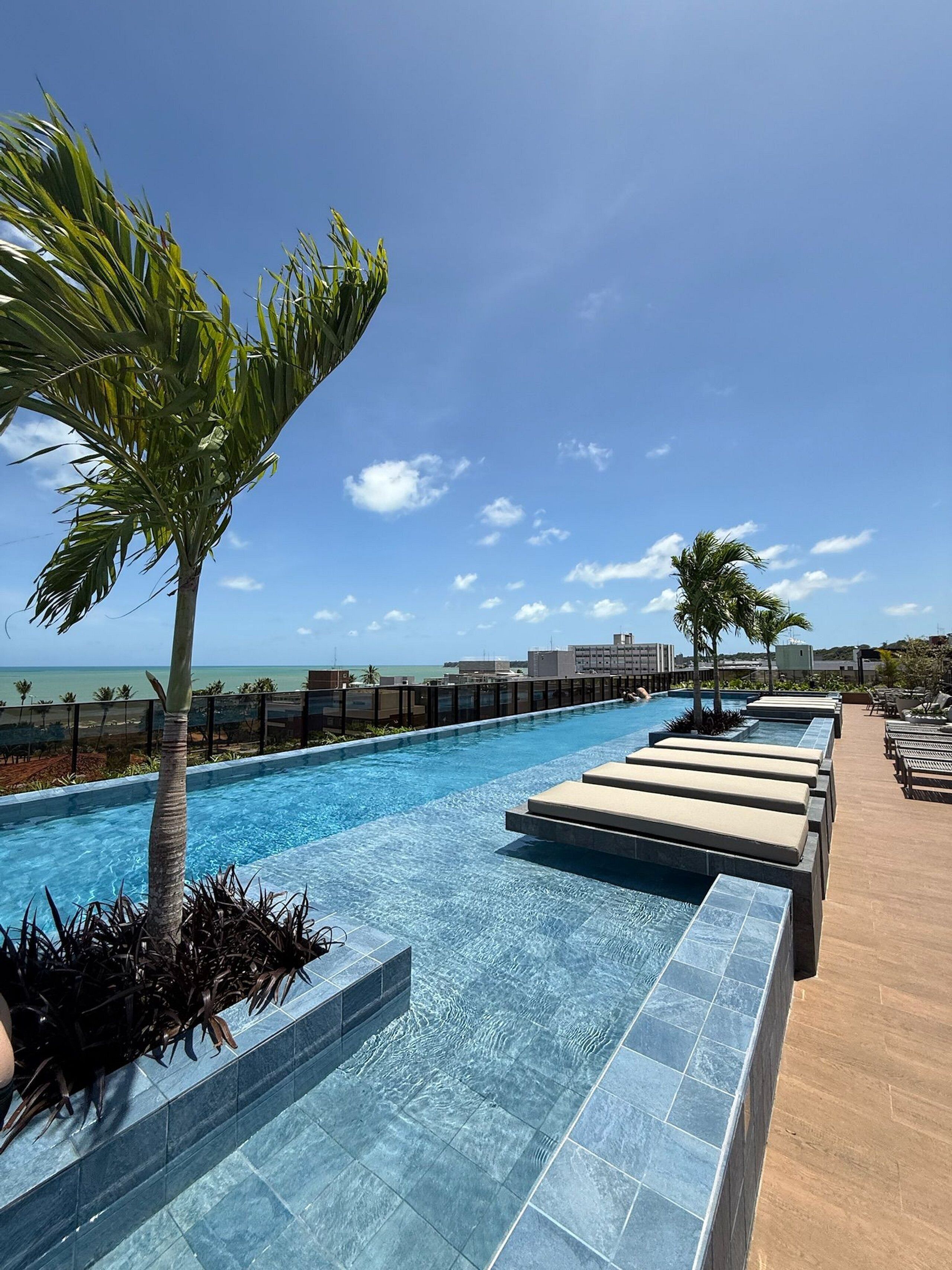 A pool area with lounge chairs and palm trees, overlooking a body of water.