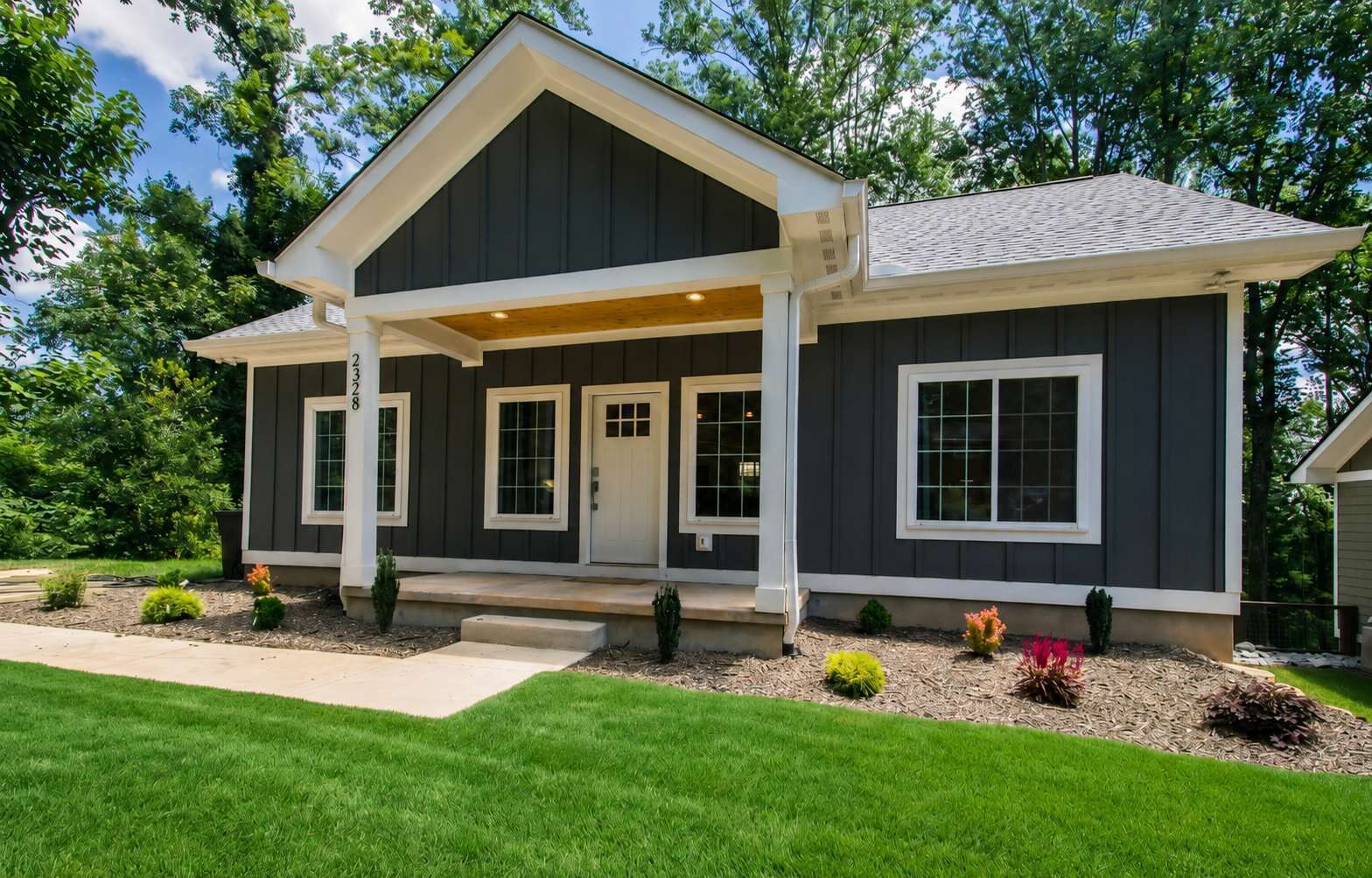 A modern two-story house with a covered porch, a front door, and a small front yard with landscaping.