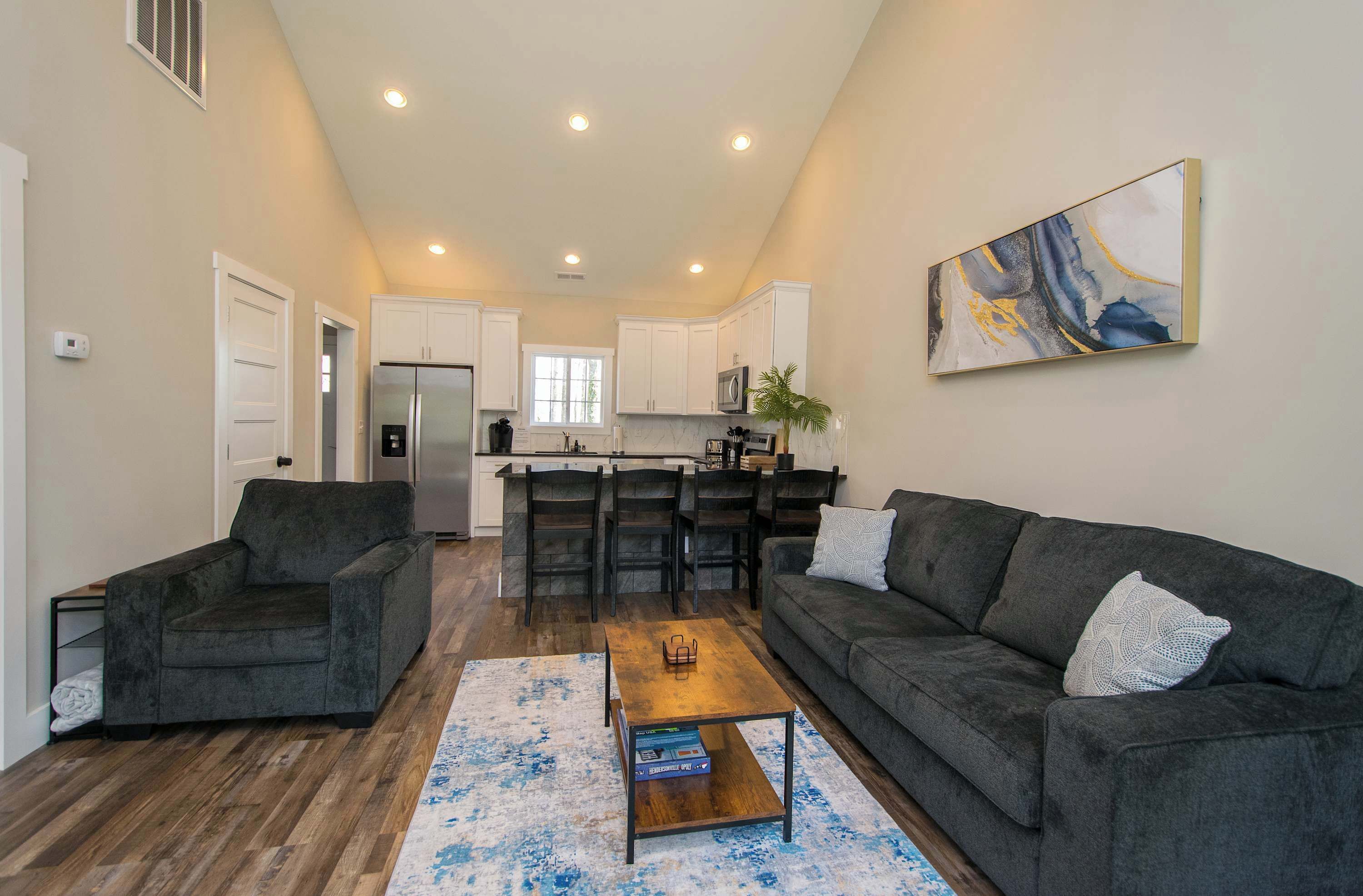 A modern living room with a sofa, armchair, coffee table, and a painting on the wall.
