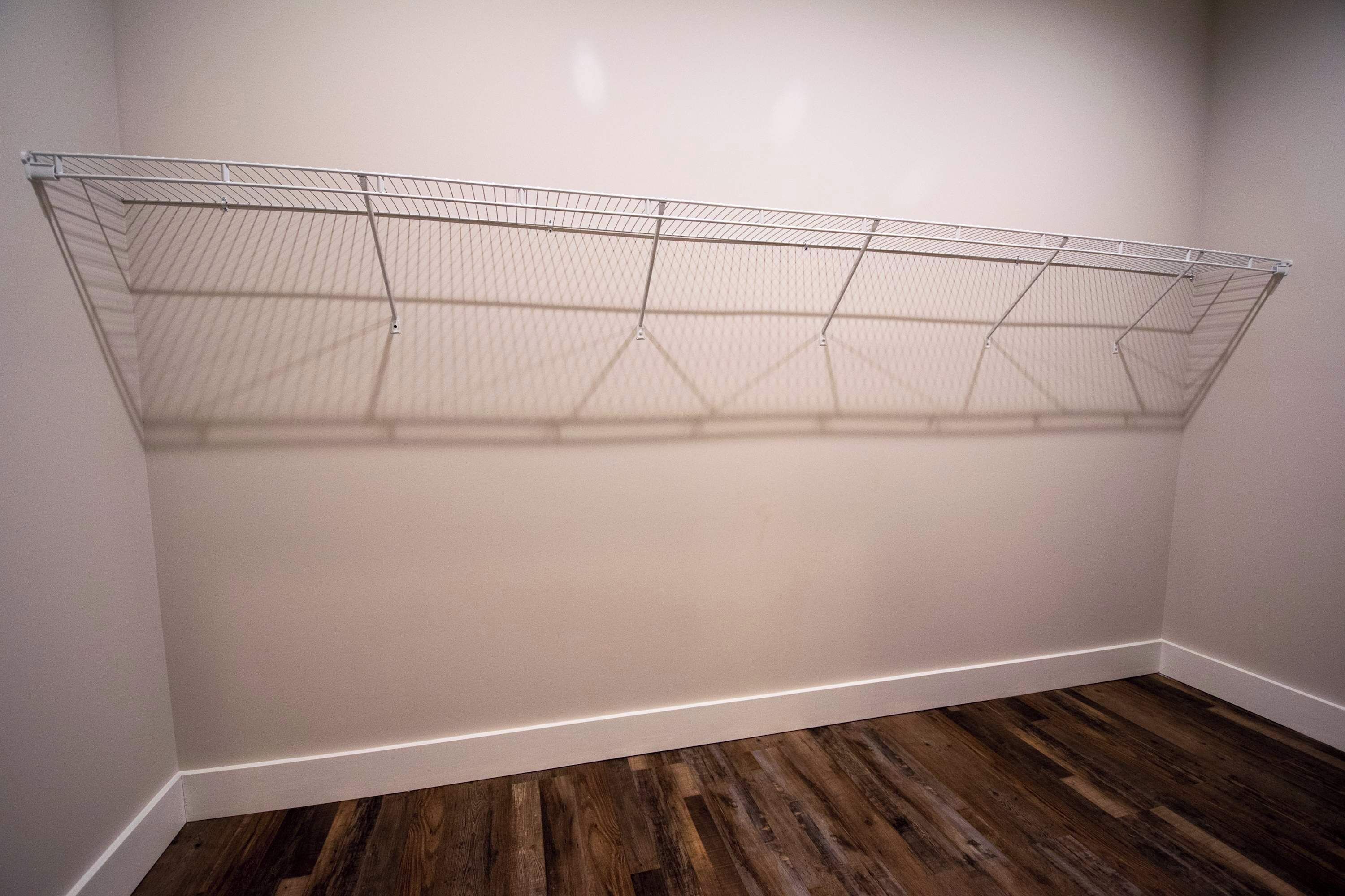 A room with a wire shelving unit against the wall and a wooden floor.