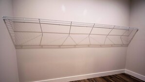 Um quarto com uma estante de aramado encostada na parede e piso de madeira.