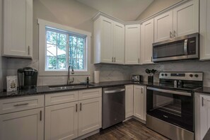 A modern kitchen with white cabinets, a built-in microwave, a stainless steel oven, and a dishwasher. - Modern Upper Retreat II | 2 Suites + Free Tix (Hendersonville)