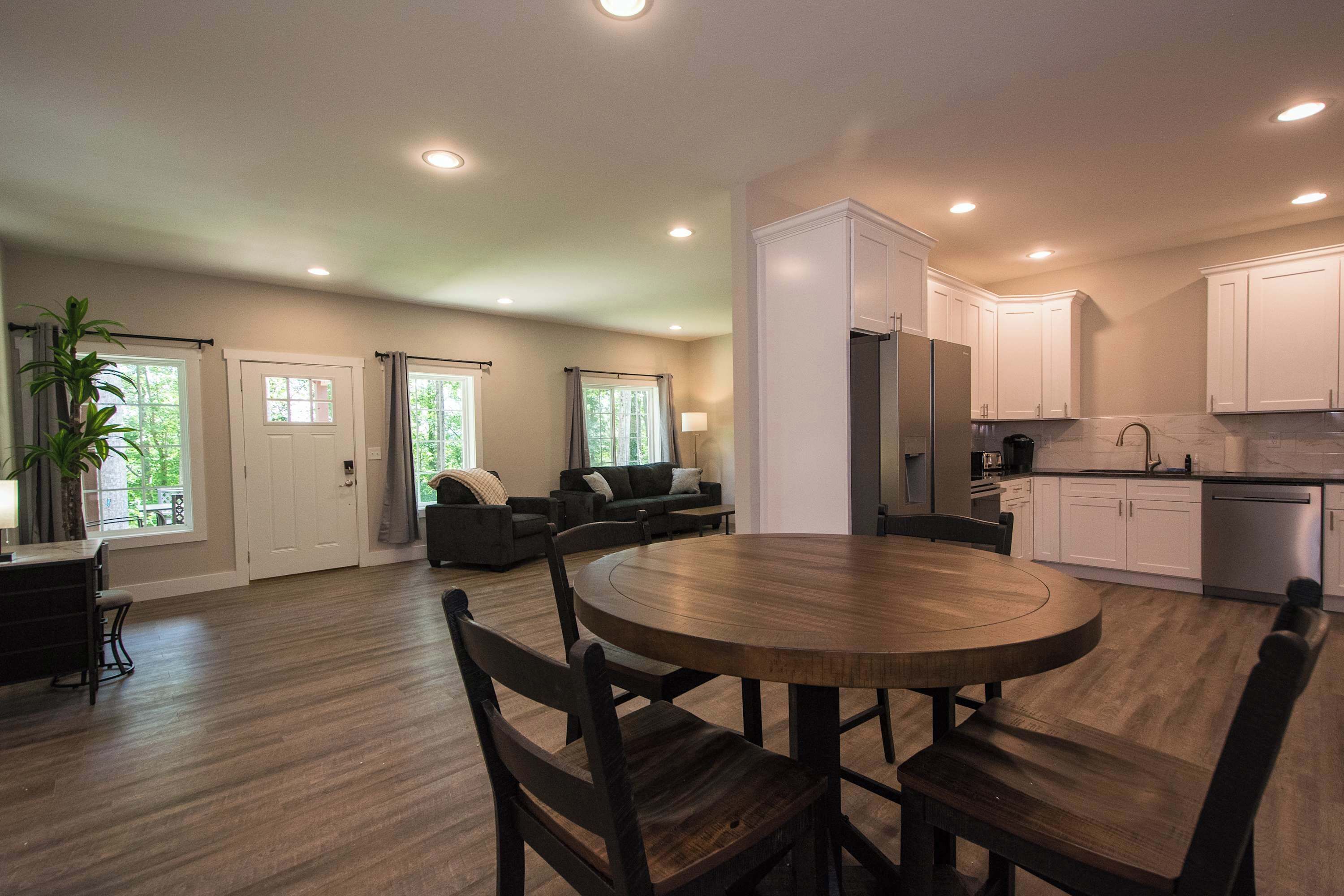 A spacious living area with a dining table, dark wooden chairs, a sofa, and a kitchen with white cabinets and stainless steel appliances.