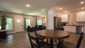 A spacious living area with a dining table, dark wooden chairs, a sofa, and a kitchen with white cabinets and stainless steel appliances.