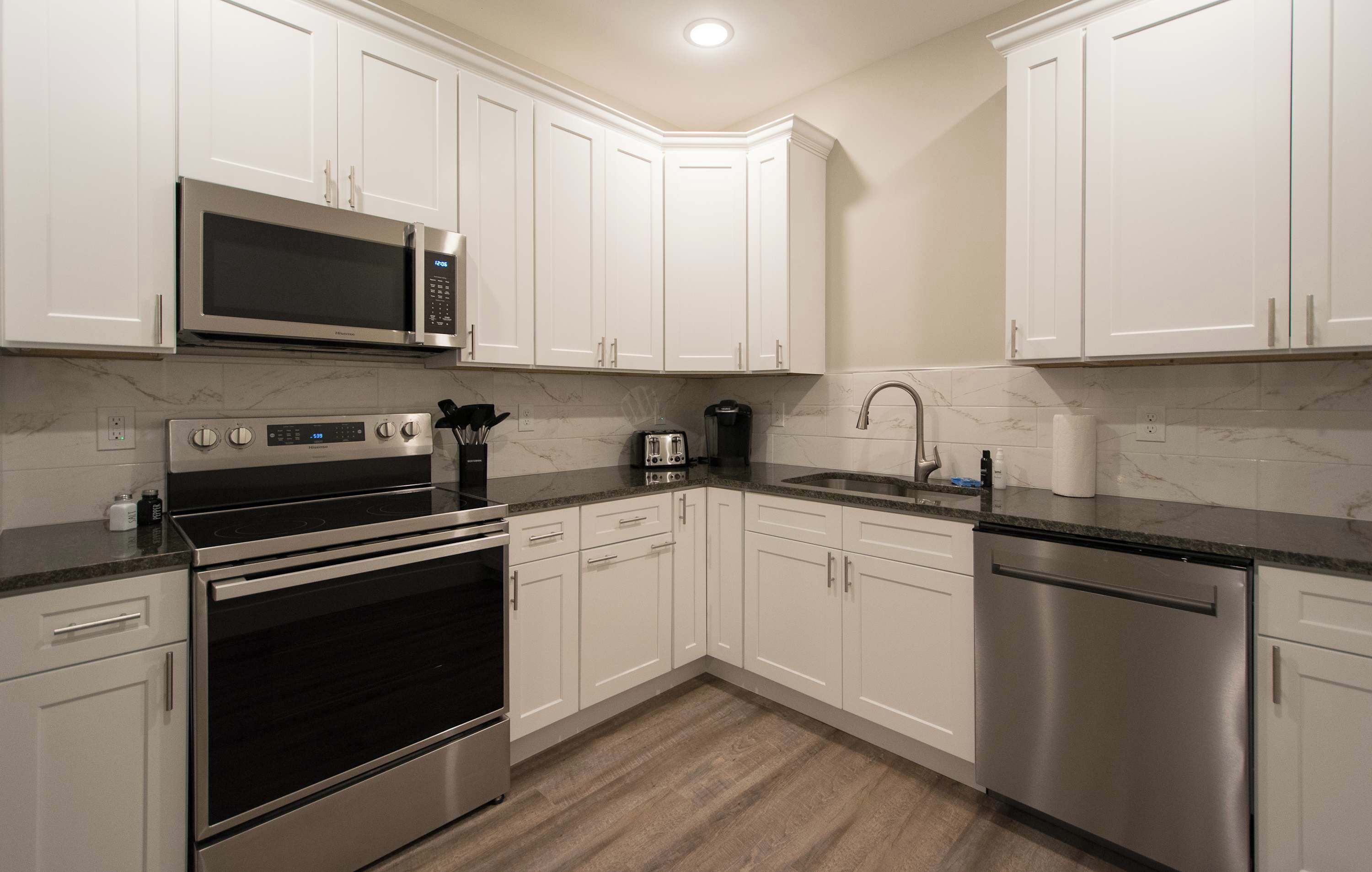 A modern kitchen with white cabinets, stainless steel appliances, a microwave, stove, toaster, and dishwasher.