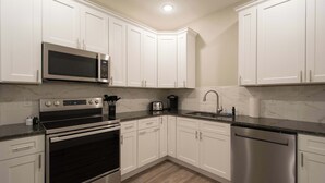 Una cocina moderna con alacenas blancas, electrodomésticos de acero inoxidable, microondas, estufa, tostadora y lavavajillas.