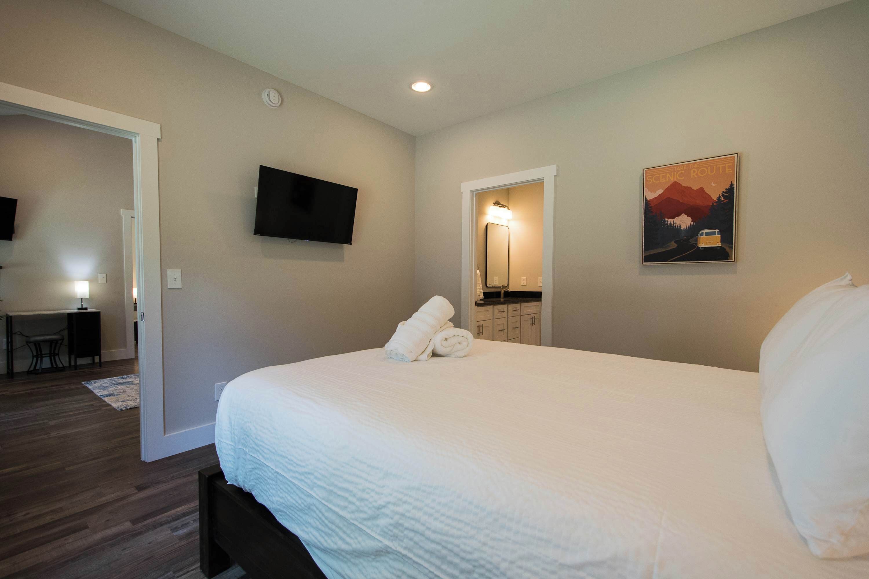 A hotel room with a bed, a flat-screen TV, a painting, and a desk with a lamp.