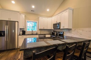 A modern kitchen with white cabinets, stainless steel appliances, and a large island with bar stools. - Druid Hills Retreat II | Sleeps 8 | Free Tix (Hendersonville)