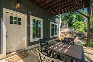 Un patio couvert avec une table et des chaises, un mur en pierre et une terrasse en bois agrémentée d’un paillasson.