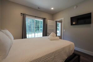 A bedroom with a bed, a TV mounted on the wall, and a window with curtains. - Druid Hills Retreat II | Sleeps 8 | Free Tix (Hendersonville)
