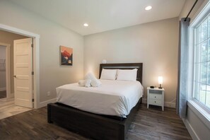 A bedroom with a bed, a nightstand, a wall clock, and a window. - Druid Hills Retreat II | Sleeps 8 | Free Tix (Hendersonville)