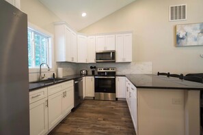 A modern kitchen with white cabinetry, a stainless steel refrigerator, a microwave, an oven, and a large island with a sink. - Druid Hills Retreat II | Sleeps 8 | Free Tix (Hendersonville)