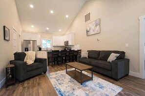 A modern living room with two sofas, a coffee table, and a kitchen in the background. - Druid Hills Retreat II | Sleeps 8 | Free Tix (Hendersonville)