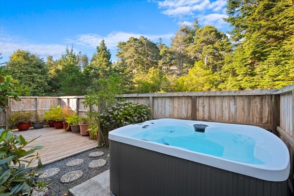 Een hottub in een achtertuin met een houten terras, omringd door potplanten en een houten schutting.