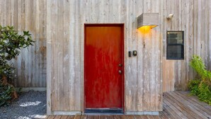 A wooden building with a red door, a small window with blinds, and a light fixture above the door. - 2BR w/Ocean View & Hot Tub, Near Black Point Beach (Sea Ranch)