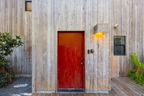 A wooden building with a red door, a small window with blinds, and a light fixture above the door. - 2BR w/Ocean View & Hot Tub, Near Black Point Beach (Sea Ranch)