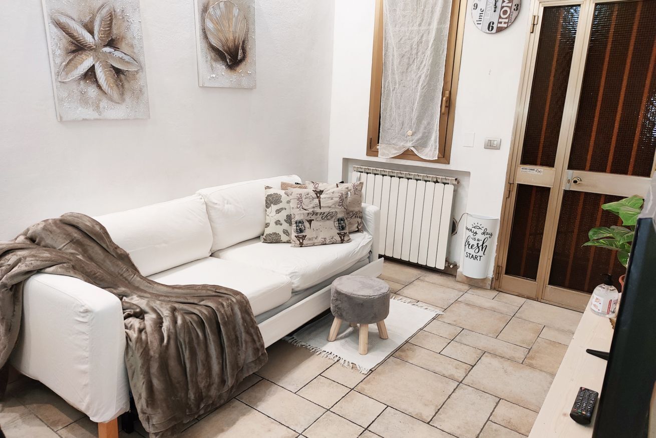 A cozy living room with a white sofa, decorative pillows, a small stool, and a radiator.