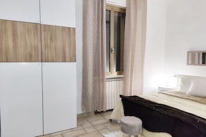 A bedroom with a bed, a wardrobe, a radiator, and a window with curtains. - UR NEST Pisano, 1 bedroom (Bologna)
