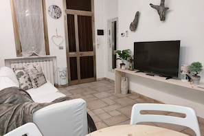 A living room with a sofa, a television, a small table, and a white chair. - UR NEST Pisano, 1 bedroom (Bologna)