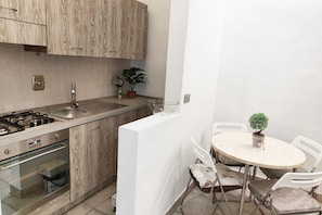 A compact kitchen with a gas stove, sink, and oven, adjacent to a dining area with a round table and chairs. - UR NEST Pisano, 1 bedroom (Bologna)