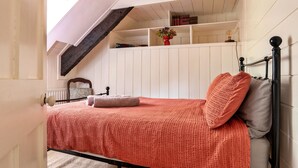 A bedroom with a sloped ceiling, a bed with a red blanket, a wooden headboard, and a small shelf with books and a vase. - Scenic Dales Hut With Hot Tub for 2 (Dolgellau)