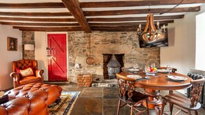A rustic dining area with a stone fireplace, wooden furniture, and a red door. - Scenic Dales Hut With Hot Tub for 2 (Dolgellau)