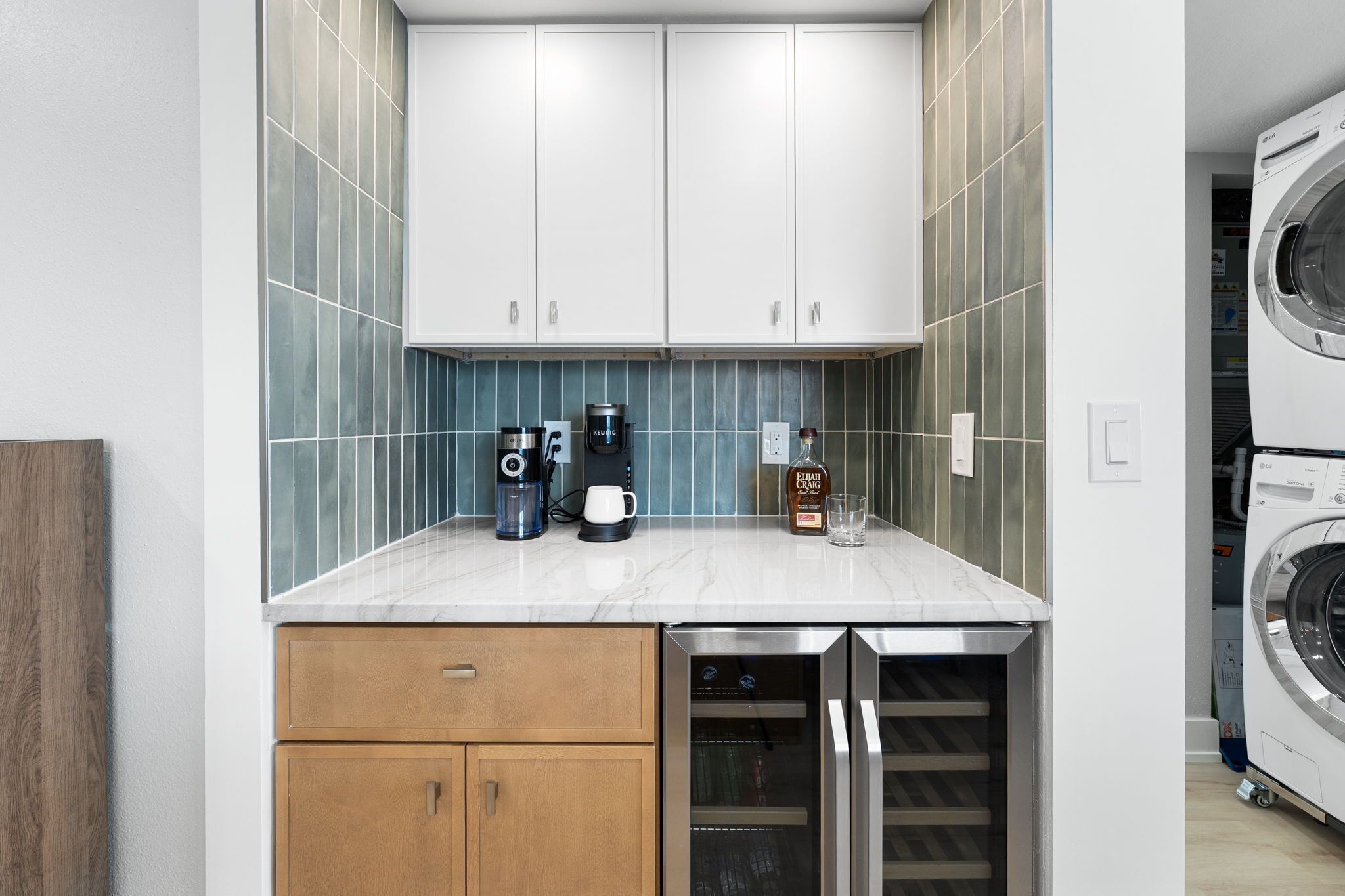 Een compacte keuken met witte kastjes, een koffiezetapparaat, een fles whiskey en een wasmachine.