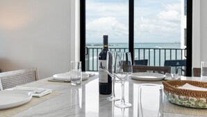 A dining table set for two with a bottle of wine, two glasses, and a woven basket. - Punta Rassa Luxe Waterfront w/ Panoramic Views, Gorgeous Sunsets, Pool, Hot Tub (Fort Myers)
