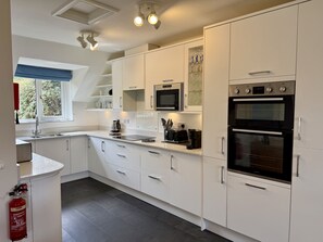 A modern kitchen with white cabinetry, a built-in microwave, a stove, and a sink. - Caldarvan - sleeps 8 guests  in 4 bedrooms (Wadebridge)