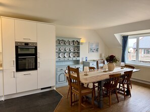A modern kitchen with white cabinetry, a dining table with wooden chairs, and a wall of decorative plates. - Caldarvan - sleeps 8 guests  in 4 bedrooms (Wadebridge)