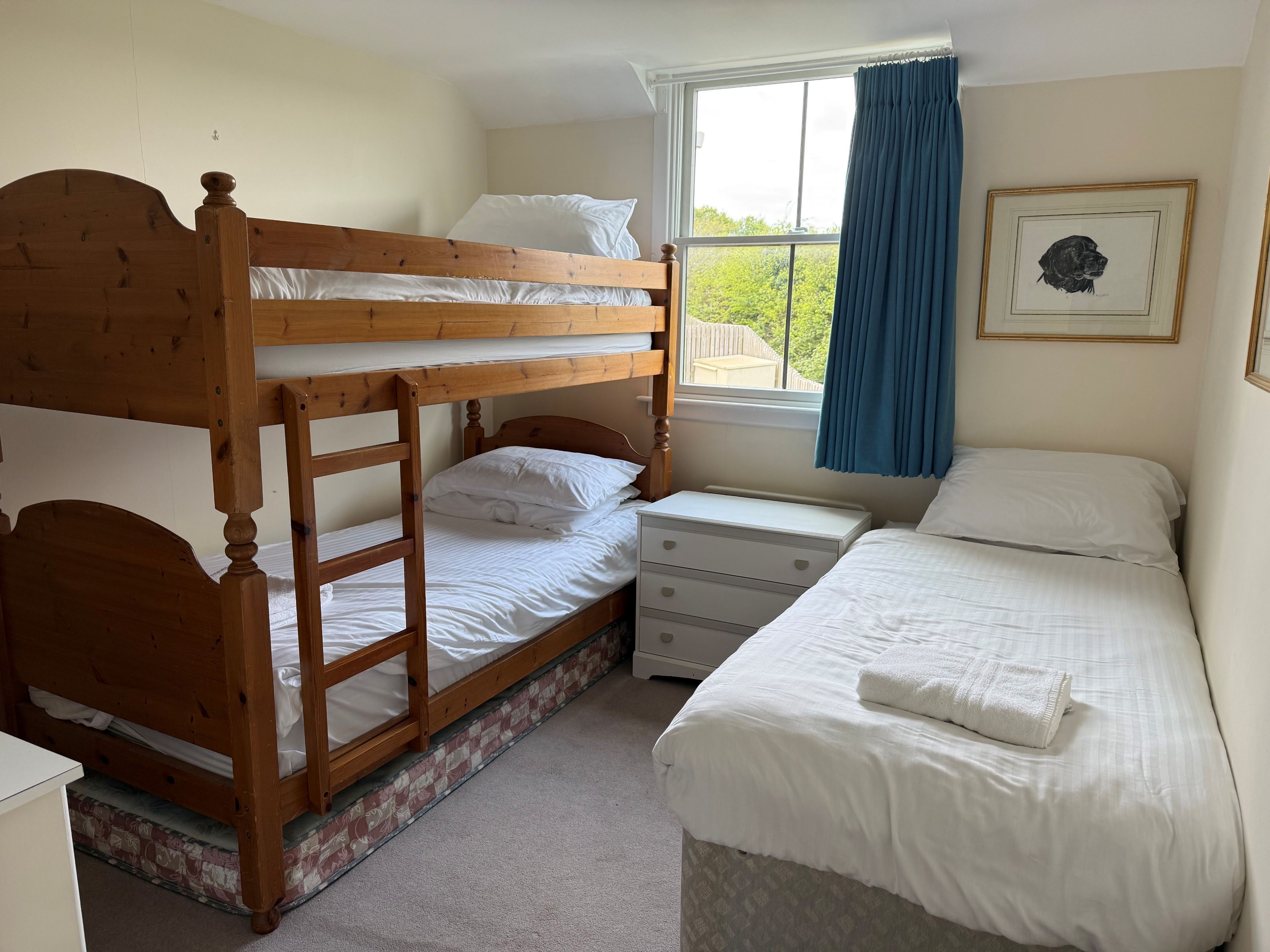 A bedroom with a bunk bed, a single bed, a nightstand, and a window with curtains.