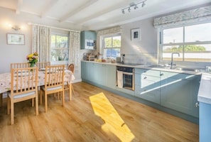 Eine moderne Küche mit Essbereich, ausgestattet mit Holzmöbeln, einem Backofen und einem großen Fenster für natürliches Licht.