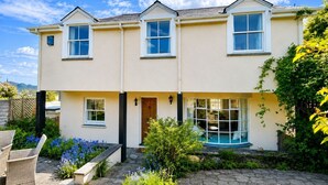 A two-story house with a front porch, a small garden with flowers, and a clear blue sky. - Cherry Tree Cottage - sleeps 6 guests  in 3 bedrooms (St Minver)