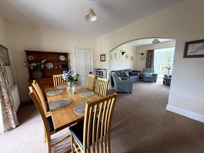 A dining area with a wooden table and chairs, a vase with flowers, and a bookshelf with decorative plates. - Broad Park-Sleeps 11 in 6 Bedrooms (Rock)